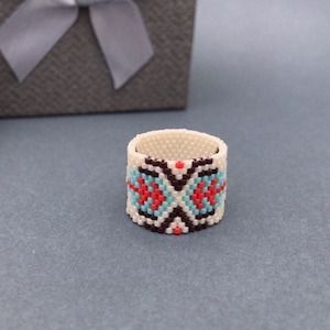 May include: A white beaded ring with a geometric pattern in shades of brown, blue, and orange.