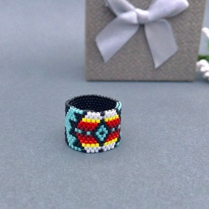 Op de afbeelding: Een kralenring met een geometrisch patroon in turquoise, rood, geel, wit en zwart.