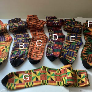 May include: A collection of colorful socks with geometric patterns in shades of orange, green, yellow, and purple. The socks are arranged on a white surface, showcasing their vibrant designs. The socks are made of a soft material and are perfect for everyday wear.