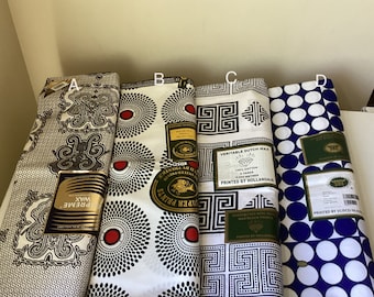 Puede incluir: Cuatro muestras de tela diferentes con varios patrones. La primera muestra tiene un patrón paisley blanco y negro con el texto "Supreme Wax Holland" impreso en la parte inferior. La segunda muestra tiene un fondo blanco con círculos negros y rojos. La tercera muestra tiene un fondo blanco con un patrón geométrico blanco y negro. La cuarta muestra tiene un fondo blanco con lunares azules. Todas las muestras tienen una etiqueta verde con texto impreso.