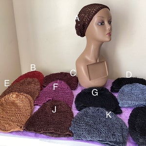 May include: A collection of crocheted hair snoods in various colors, including brown, burgundy, purple, black, and gray. The snoods are displayed on a mannequin head and a table, showcasing their texture and design.