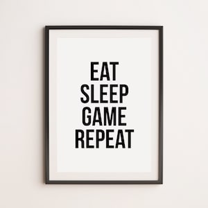 May include: Black and white framed print with the text "Eat Sleep Game Repeat" in a bold font.