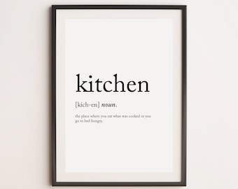 May include: A framed print with the word "kitchen" in a bold, black font. Below the word is a definition, also in black, that reads "the place where you eat what was cooked or you go to bed hungry."