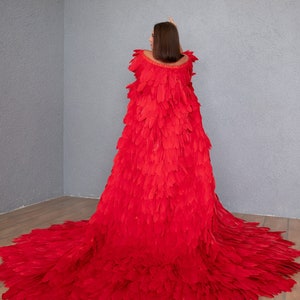 May include: A woman wearing a long, red feather dress. The dress is made of many individual feathers that are sewn together to create a flowing, dramatic look.