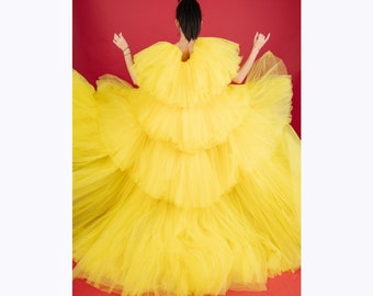 May include: A woman wearing a bright yellow tulle dress with multiple layers. The dress is full and flowing, and the woman is standing with her back to the camera.