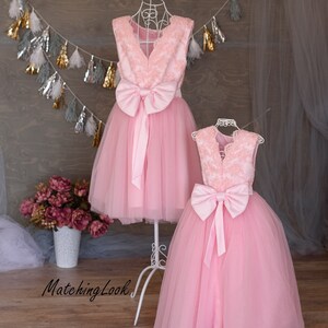 Puede incluir: Dos vestidos de tul rosa con corpi&ntilde;os de encaje y lazos de sat&eacute;n. Los vestidos est&aacute;n en maniqu&iacute;es sobre un fondo de madera.