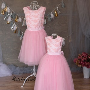 Puede incluir: Dos vestidos de tul rosa con detalles de encaje y cinturas de sat&eacute;n. Los vestidos est&aacute;n en maniqu&iacute;es sobre un fondo de madera.