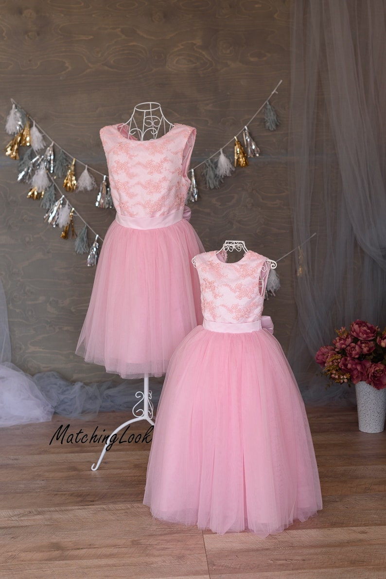 Puede incluir: Dos vestidos de tul rosa con detalles de encaje y cinturas de sat&eacute;n. Los vestidos est&aacute;n en maniqu&iacute;es sobre un fondo de madera.