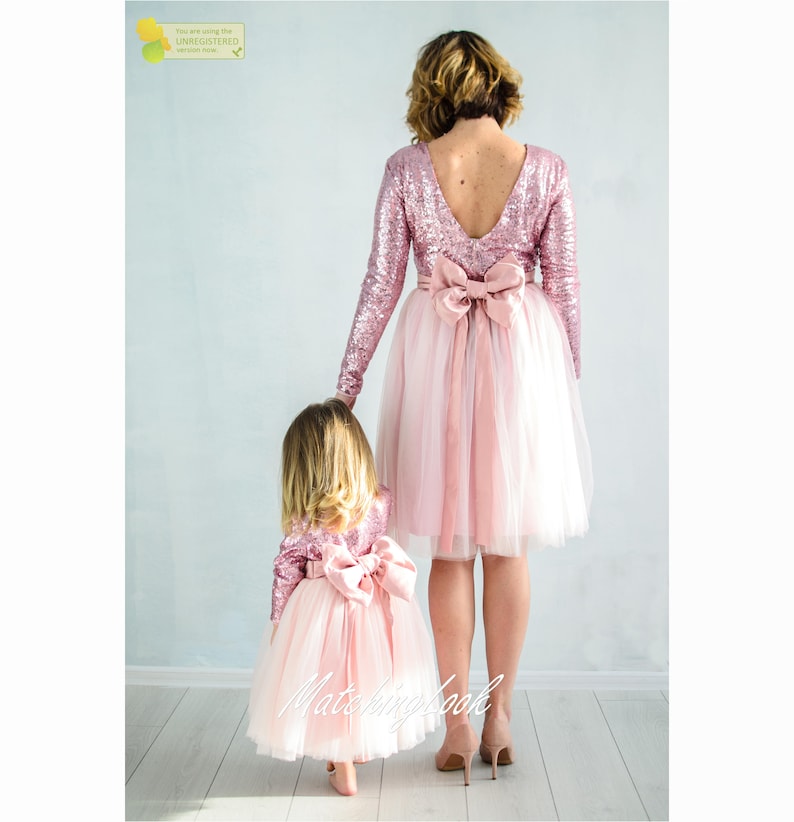 May include: Two people wearing matching pink sequin and tulle dresses with long sleeves and pink bows. The dresses have a tulle skirt and a sequin bodice.