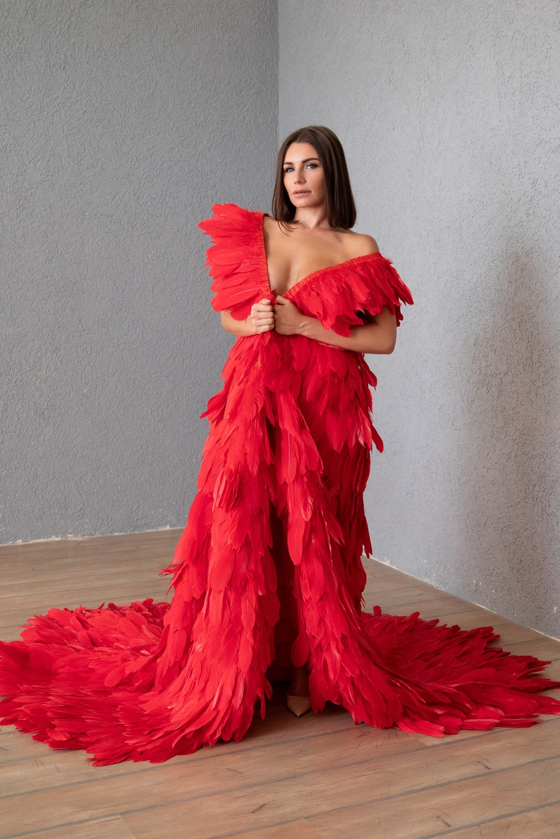 May include: A woman wearing a red feather dress with a long train. The dress is made of many layers of feathers and has a deep V-neckline.