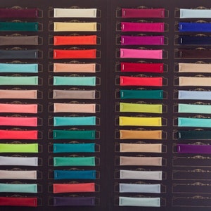 Pu&ograve; includere: Una cartella colori con 20 righe di campioni di tessuto. Ogni riga ha 4 campioni di colori diversi. I campioni sono disposti in una griglia. I colori includono rosso, blu, verde, giallo, arancione, viola, rosa, marrone, beige e bianco.