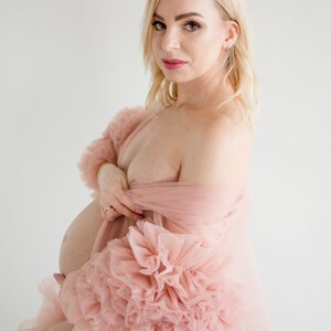 Pu&ograve; includere: Una donna incinta che indossa un abito di tulle rosa con maniche a sbuffo. L'abito &egrave; trasparente e ha una silhouette fluida.