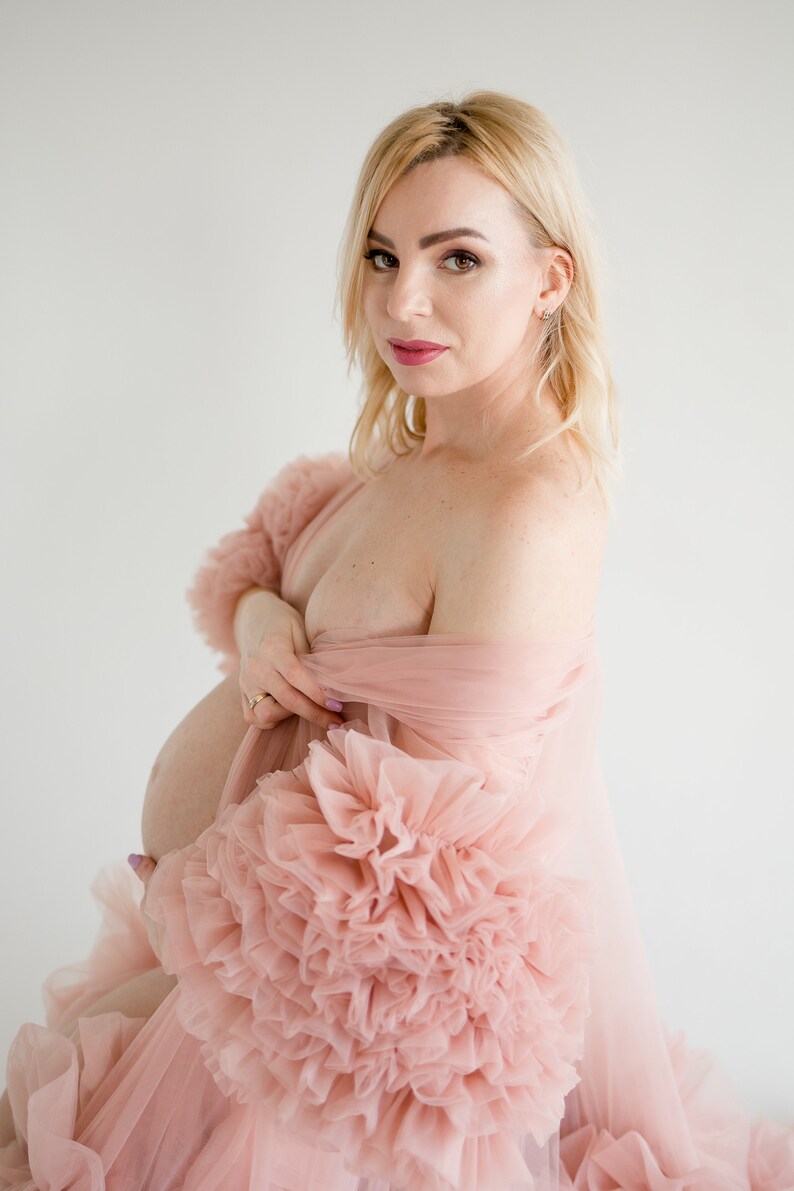 Pu&ograve; includere: Una donna incinta che indossa un abito di tulle rosa con maniche a sbuffo. L'abito &egrave; trasparente e ha una silhouette fluida.