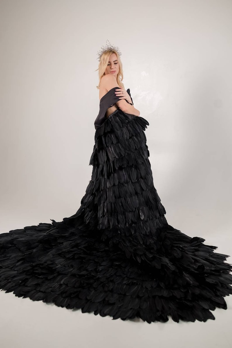 May include: A woman wearing a black feather gown and a crown. The gown is made of many layers of feathers and has a long train.