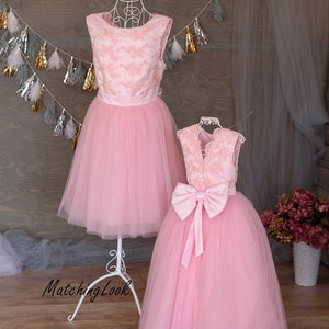 Puede incluir: Dos vestidos de tul rosa con corpi&ntilde;os de encaje. El vestido m&aacute;s grande tiene un lazo de sat&eacute;n en la espalda. Los vestidos est&aacute;n en un soporte blanco sobre un fondo de madera.