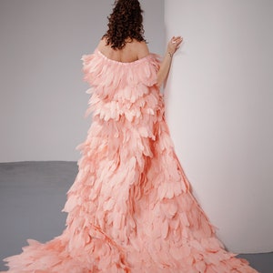 May include: A woman wearing a long, flowing pink dress made entirely of feathers. The dress is off-the-shoulder and has a train.