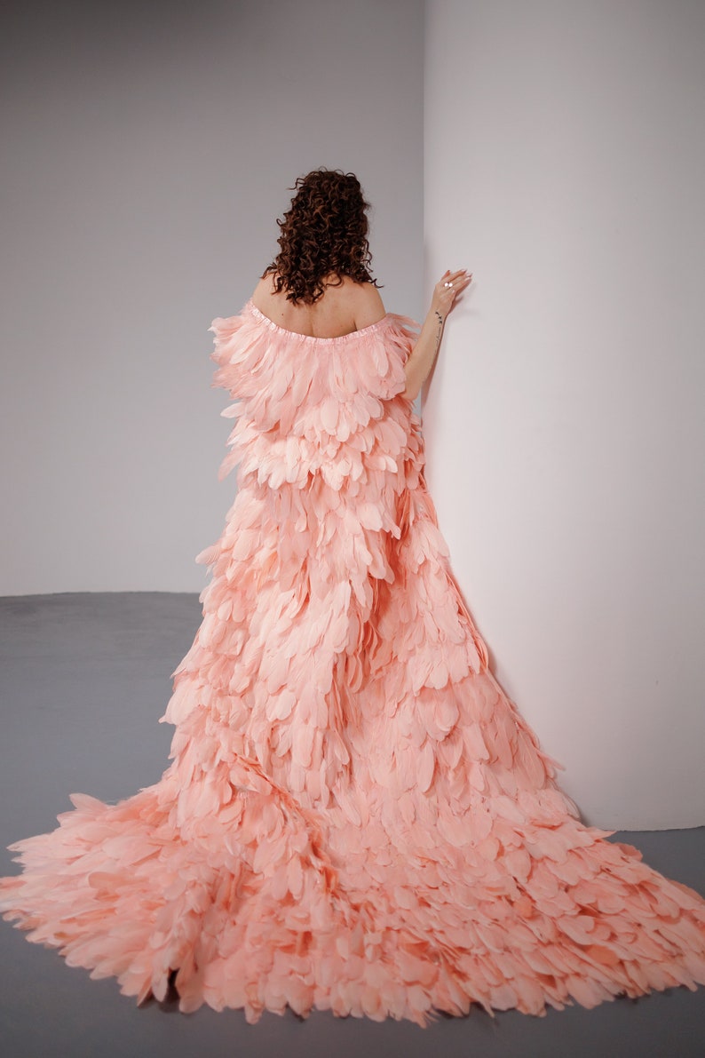 May include: A woman wearing a long, flowing pink dress made entirely of feathers. The dress is off-the-shoulder and has a train.