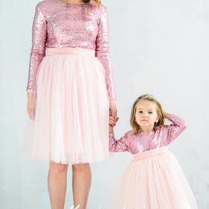 May include: A mother and daughter wearing matching pink sequin long-sleeve tops and tulle skirts. The tops have a round neckline and the skirts are full and flowy. The caption "Matching Look" is visible at the bottom of the image.