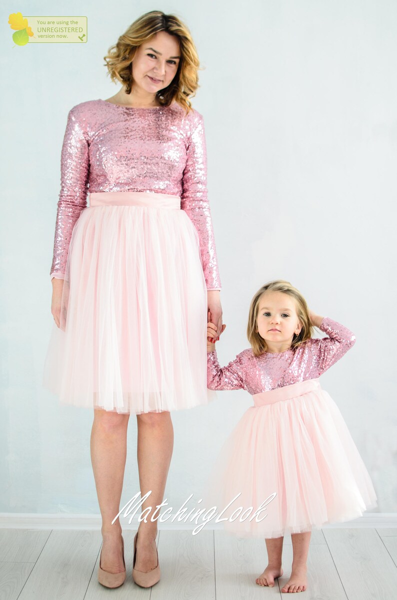May include: A mother and daughter wearing matching pink sequin long-sleeve tops and tulle skirts. The tops have a round neckline and the skirts are full and flowy. The caption "Matching Look" is visible at the bottom of the image.