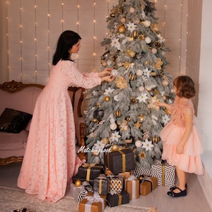 Puede incluir: Una mujer y una ni&ntilde;a peque&ntilde;a decoran un &aacute;rbol de Navidad con adornos blancos y dorados. El &aacute;rbol est&aacute; decorado con poinsettias blancas y adornos rayados dorados y negros. Hay regalos envueltos en papel de regalo negro, blanco y dorado en la base del &aacute;rbol.