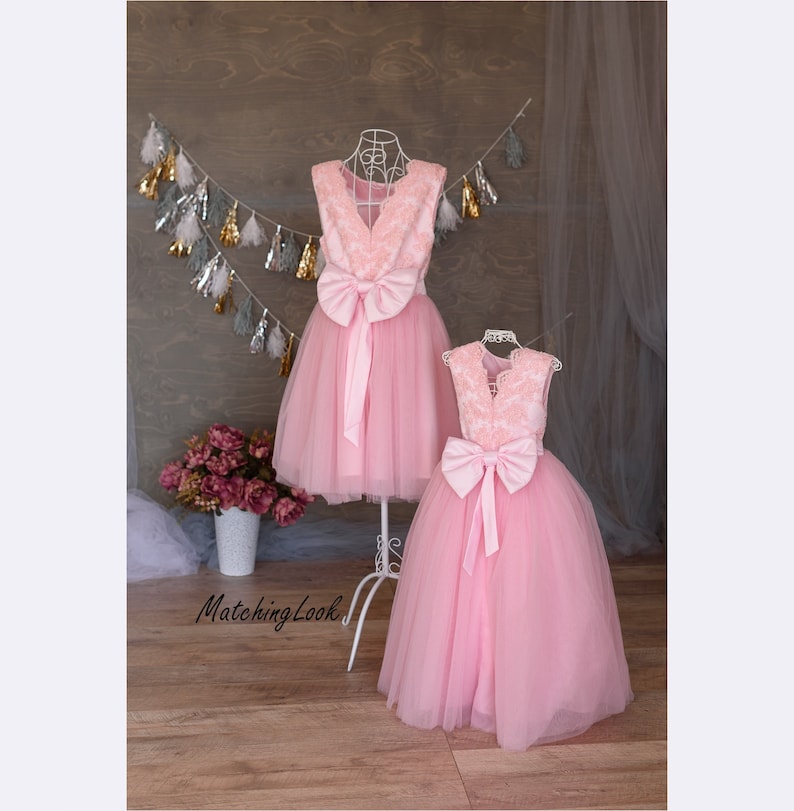 Puede incluir: Dos vestidos de tul rosa con corpi&ntilde;os de encaje y lazos de sat&eacute;n. El vestido de la izquierda es m&aacute;s corto que el vestido de la derecha.