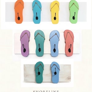 May include: A collection of colorful flip-flop shaped wall hooks. The hooks are in various colors, including orange, blue, yellow, green, purple, teal, light blue, and coral. Each hook has a black hook and rope-like thong detail. The Shoreline Studio logo is at the bottom.