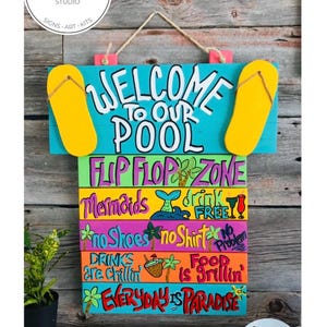May include: A multi-colored wooden sign with a rope hanger featuring the text WELCOME TO OUR POOL, FLIP FLOP ZONE, Mermaids drink FREE, no Shoes no Shirt no Problem, DRINKS are chillin FOOD is grillin, and EVERYDAY IS PARADISE with painted flip-flops.