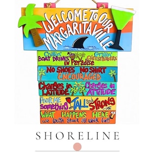 May include: A colorful wooden sign with the text "WELCOME TO OUR MARGARITAVILLE." The sign features a palm tree, a margarita glass, and various phrases like "Boat Drinks in Paradise" and "What Happens Here." The sign is from Shoreline Studio.