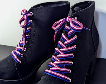 May include: A pair of black heeled ankle boots with white, pink, and blue striped laces. The laces are tied in a criss-cross pattern.