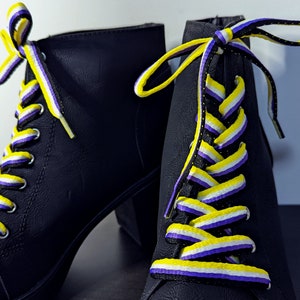 May include: A pair of black heeled boots with yellow, white and purple shoelaces. The laces are tied in a criss-cross pattern.