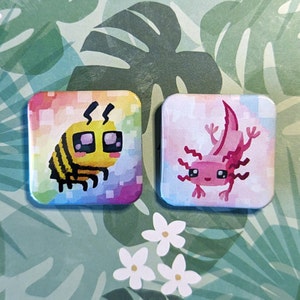 May include: Two square pins with colourful backgrounds. One pin features a cartoon bee with yellow and black stripes and a pink and blue background. The other pin features a cartoon pink axolotl with a pink and blue background.