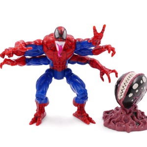 May include: A Spider-Man action figure with multiple arms, red and blue suit, and a long pink tongue. Beside it is a black and white creature with a toothy grin, on a maroon base. A collectible toy.