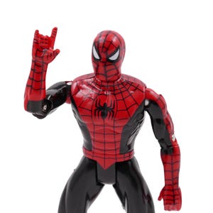 May include: A red and black Spider-Man action figure with a web design on the chest and arms. The figure is posed with one arm raised, hand in a gesture. The figure is on a white background.