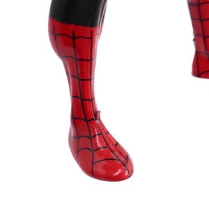 May include: Close-up of a red and black Spider-Man costume leg and foot. The red sections have a black web pattern. The black section is at the top of the leg. The foot is pointing down.