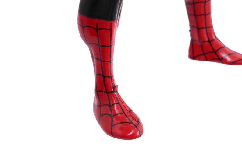 May include: Close-up of a red and black Spider-Man costume leg and foot. The red sections have a black web pattern. The black section is at the top of the leg. The foot is pointing down.