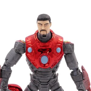 Op de afbeelding: Gedetailleerd actiefiguur van een man in een rood en grijs pantserpak. Het figuur heeft een metallic rode borstplaat met blauwe accenten en een gedetailleerd gezicht met een snor. De armen en benen zijn grijs met rode details.
