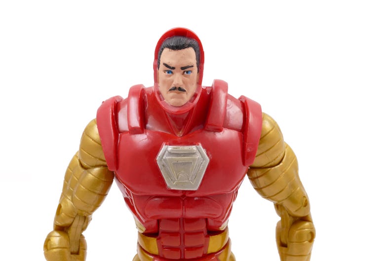May include: A close-up of an Iron Man action figure. The figure has a red and gold color scheme, with a red helmet and chest piece, and gold arms. The face is visible, with a mustache and blue eyes.