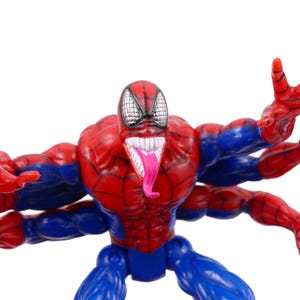 May include: A red, blue, and white action figure of a superhero with multiple arms. The figure has a red and blue costume, a white mouth with a pink tongue, and a black and white mask.
