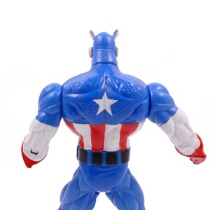 Pode incluir: Figura de a&ccedil;&atilde;o azul do Capit&atilde;o Am&eacute;rica, vista de tr&aacute;s, com uma estrela branca nas costas. A figura tem detalhes vermelhos, brancos e azuis, incluindo um cinto preto e bra&ccedil;os brancos com luvas vermelhas. Em fundo branco.