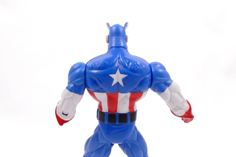 Pode incluir: Figura de a&ccedil;&atilde;o azul do Capit&atilde;o Am&eacute;rica, vista de tr&aacute;s, com uma estrela branca nas costas. A figura tem detalhes vermelhos, brancos e azuis, incluindo um cinto preto e bra&ccedil;os brancos com luvas vermelhas. Em fundo branco.