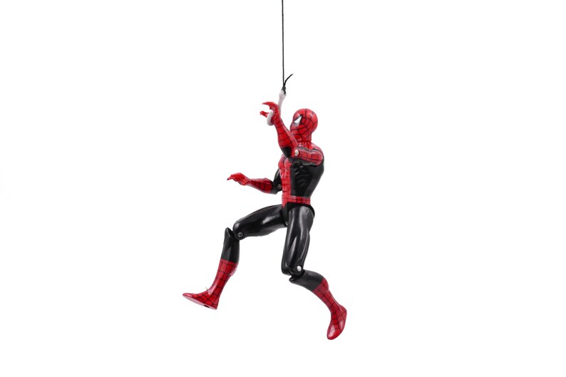 May include: A Spider-Man action figure in a dynamic pose, suspended from a black string. The figure is predominantly red and black, with a detailed mask and suit. The figure is approximately 6 inches tall.