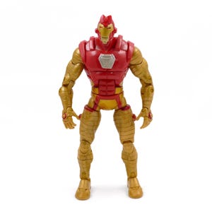 May include: A gold and red action figure of a superhero. The figure has a red chest and head, with gold arms, legs, and torso. The figure is standing upright with its arms at its sides. The figure has a silver emblem on its chest.