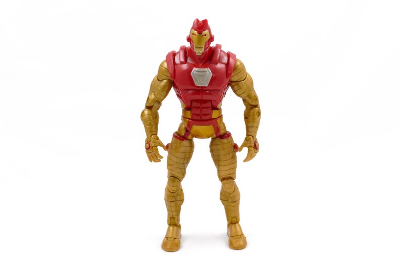 May include: A gold and red action figure of a superhero. The figure has a red chest and head, with gold arms, legs, and torso. The figure is standing upright with its arms at its sides. The figure has a silver emblem on its chest.