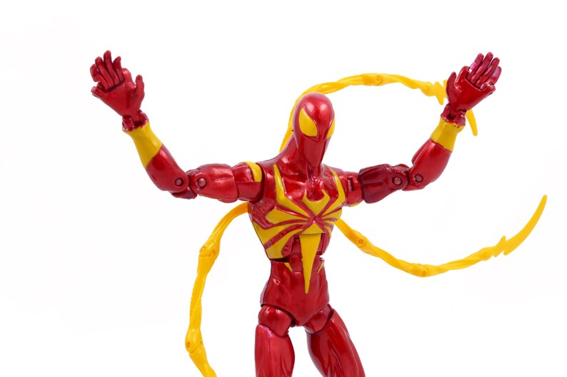 May include: Red and yellow action figure of a superhero with web-like appendages. The figure is posed with arms raised and web-like appendages extended.