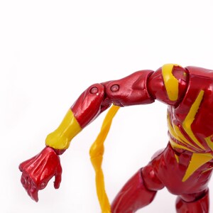 May include: A red and yellow action figure of a superhero with a web design on the chest. The figure has articulated arms and legs.