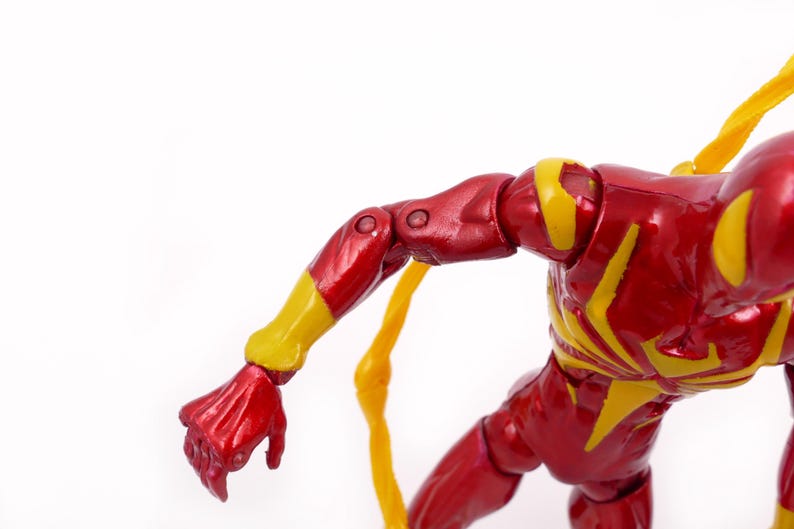 May include: A red and yellow action figure of a superhero with a web design on the chest. The figure has articulated arms and legs.