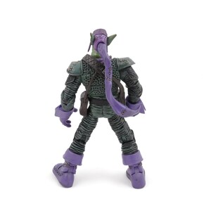 K&ouml;nnte beinhalten: Eine Green Goblin-Actionfigur, von hinten gesehen, steht auf einer wei&szlig;en Oberfl&auml;che. Die Figur ist &uuml;berwiegend gr&uuml;n und lila, mit detaillierter R&uuml;stung und einer langen, lila Kapuze. Die Figur hat eine detaillierte Textur.
