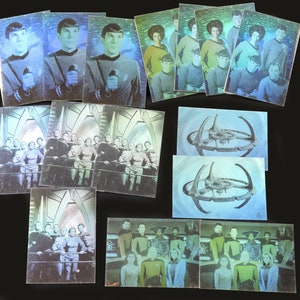 May include: A collection of vintage Star Trek trading cards featuring images of the cast and iconic scenes. The cards display characters in their uniforms and images of the Star Trek starship. The cards are arranged on a black surface.