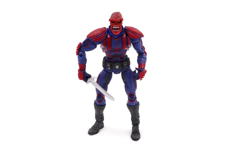May include: A Red Skull action figure, standing upright and holding a silver sword. The figure is primarily blue and red, with a detailed design. It has a red skull-shaped head and is wearing a black belt and boots. The figure is a collectible item.