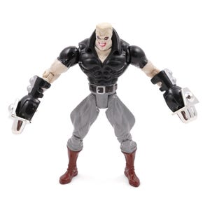 May include: A detailed action figure of a muscular character with a pale complexion, black top, gray pants, and red boots. The figure has large black gauntlets with silver accents and is posed with arms outstretched.